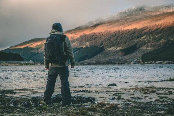 Young traveller stood on the edge of a loch in Scotland with a back-pack | by Daniel Atkins 600x400